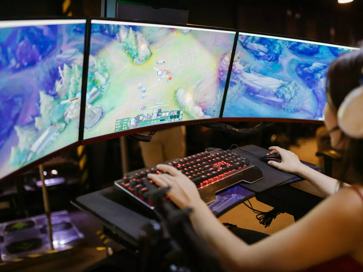 A person is playing a video game on a computer with a triple monitor setup.