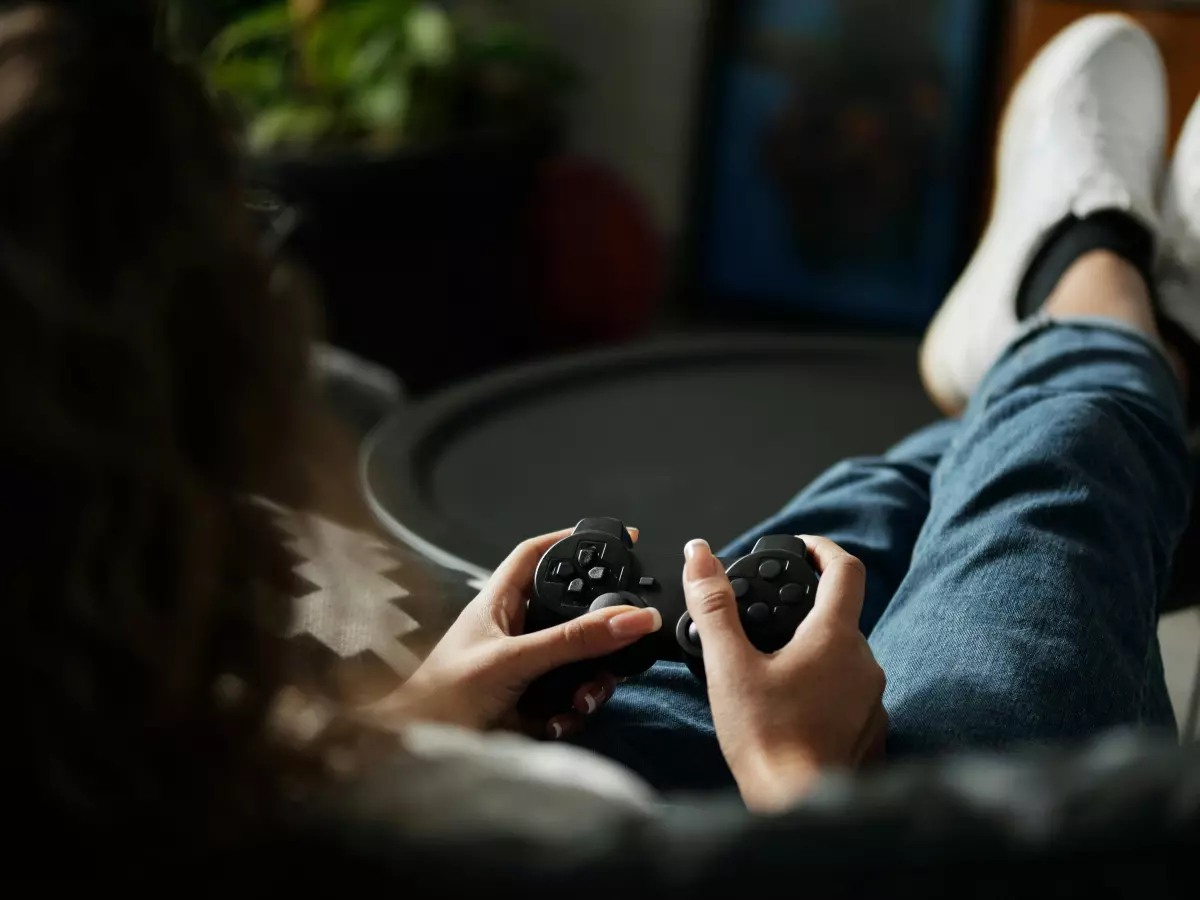 A woman is sitting on a couch and playing a video game on an Xbox controller.