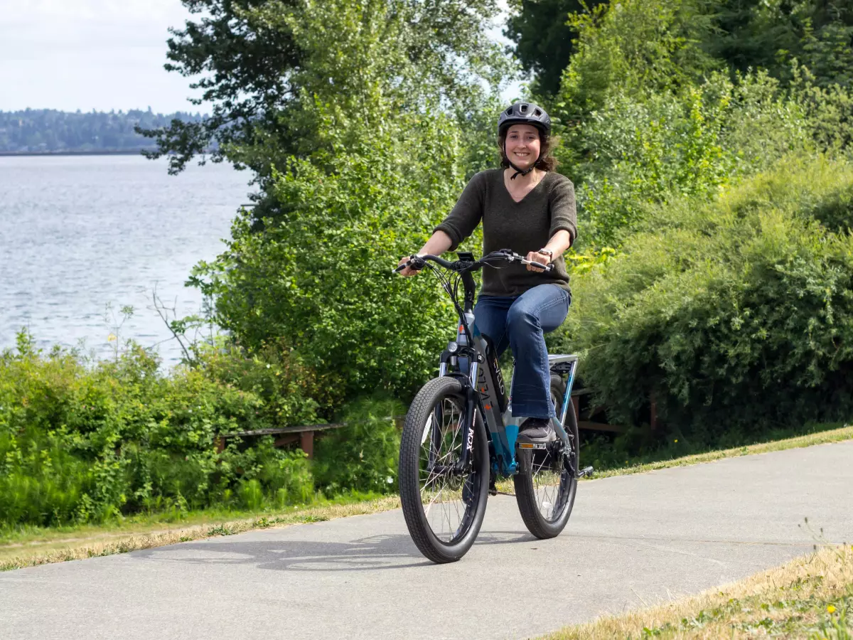 A person riding a Pedego Cargo E-Bike on a paved path near a body of water.