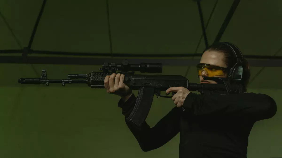 A woman in black clothing aiming a rifle at an indoor shooting range.