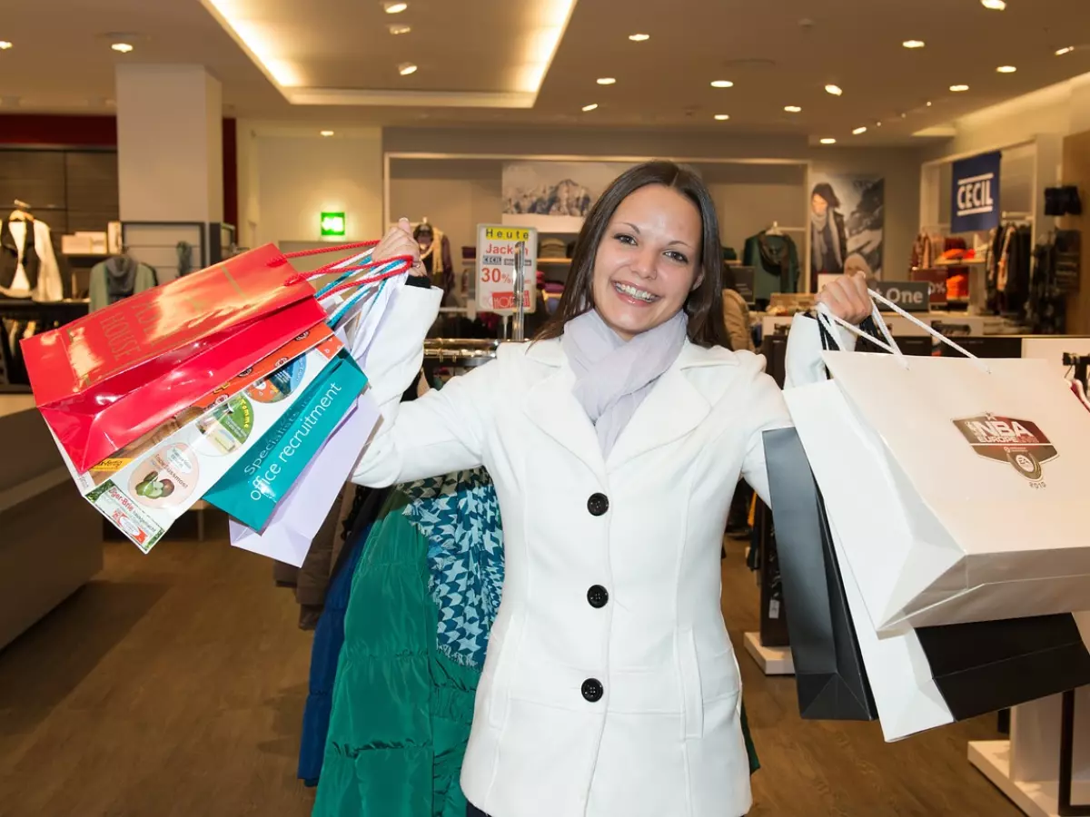 A woman with a white jacket holding multiple shopping bags in a store.