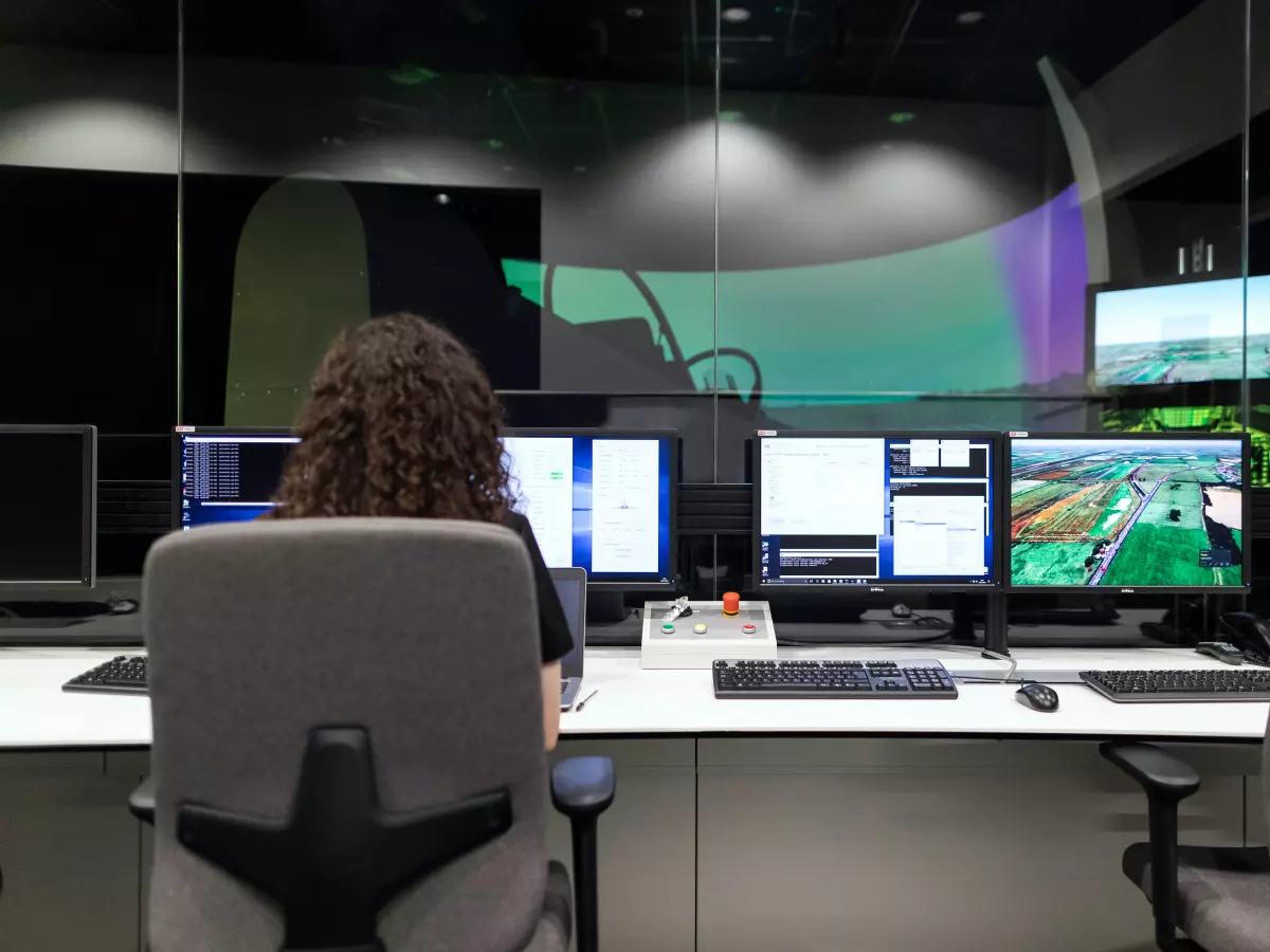 A woman is sitting in front of a computer in a large room. The room is filled with servers and other equipment.