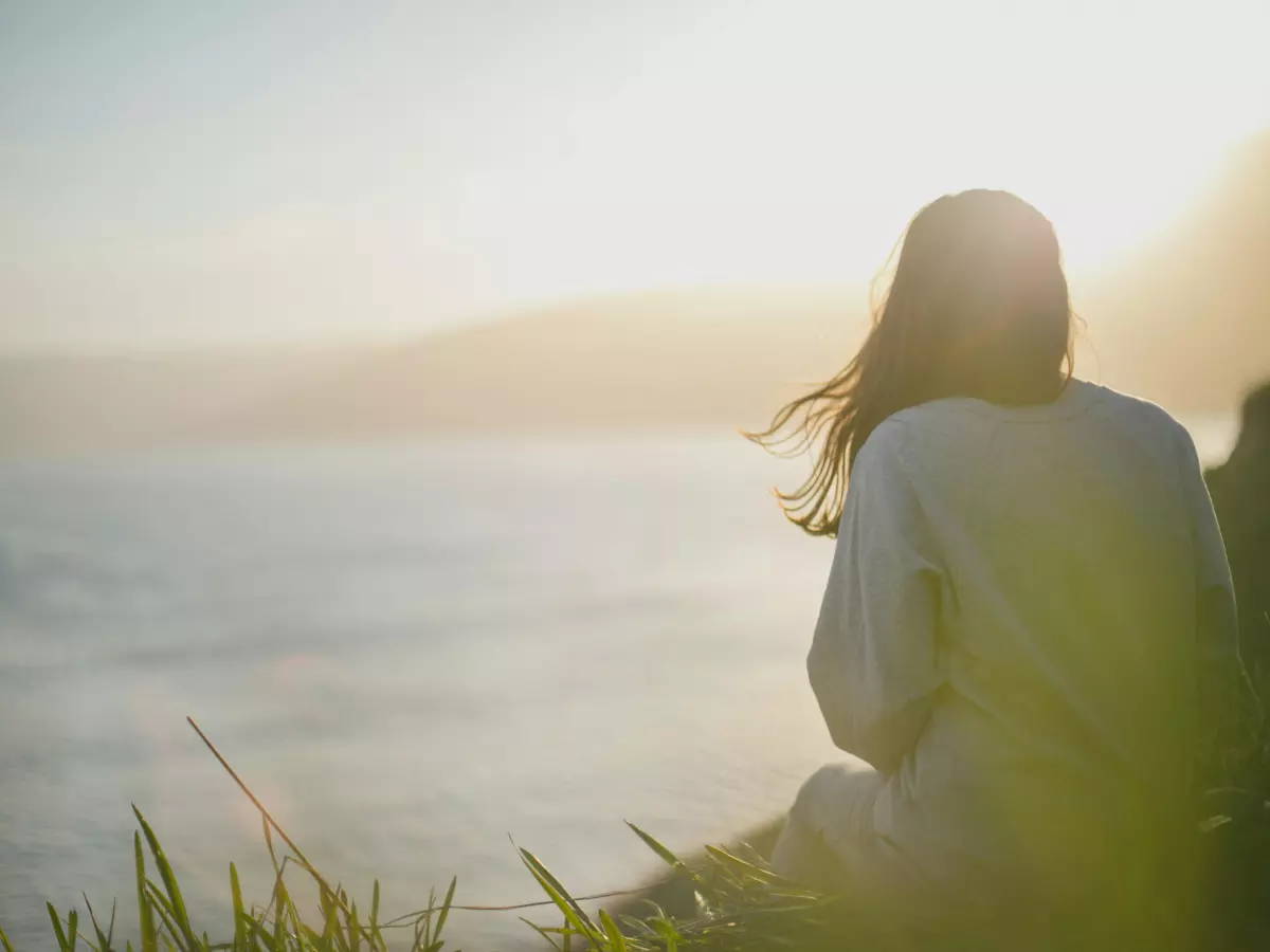 A woman sits on a cliff looking out at the ocean. 