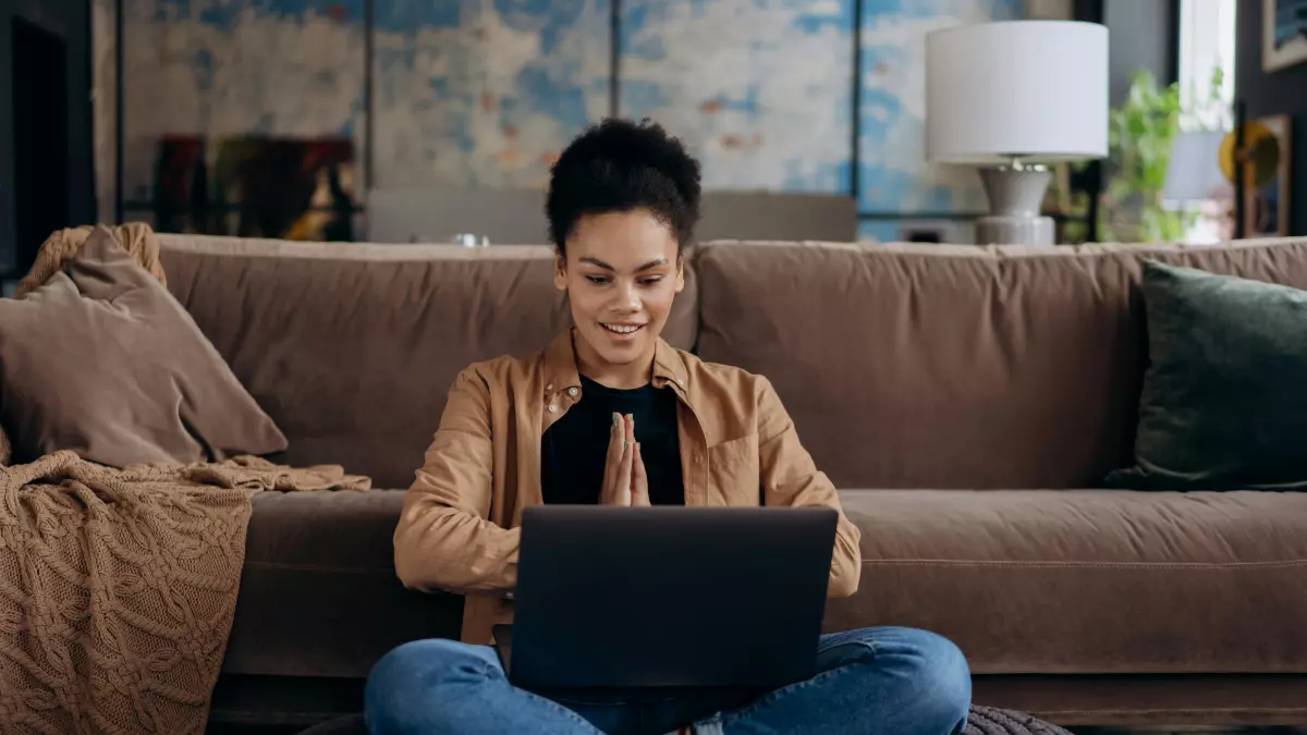 A woman sits on the floor with a laptop and smiles.