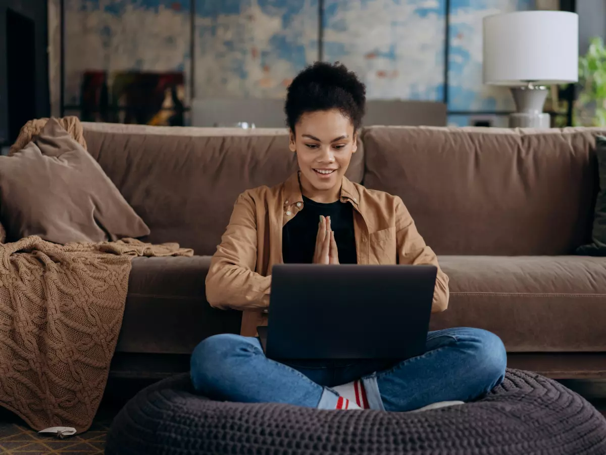 A woman sits on the floor with a laptop and smiles.