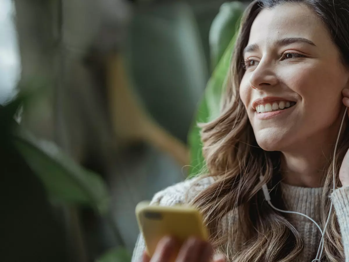 A young woman listens to music on her smartphone with headphones on. She is smiling, enjoying the music.