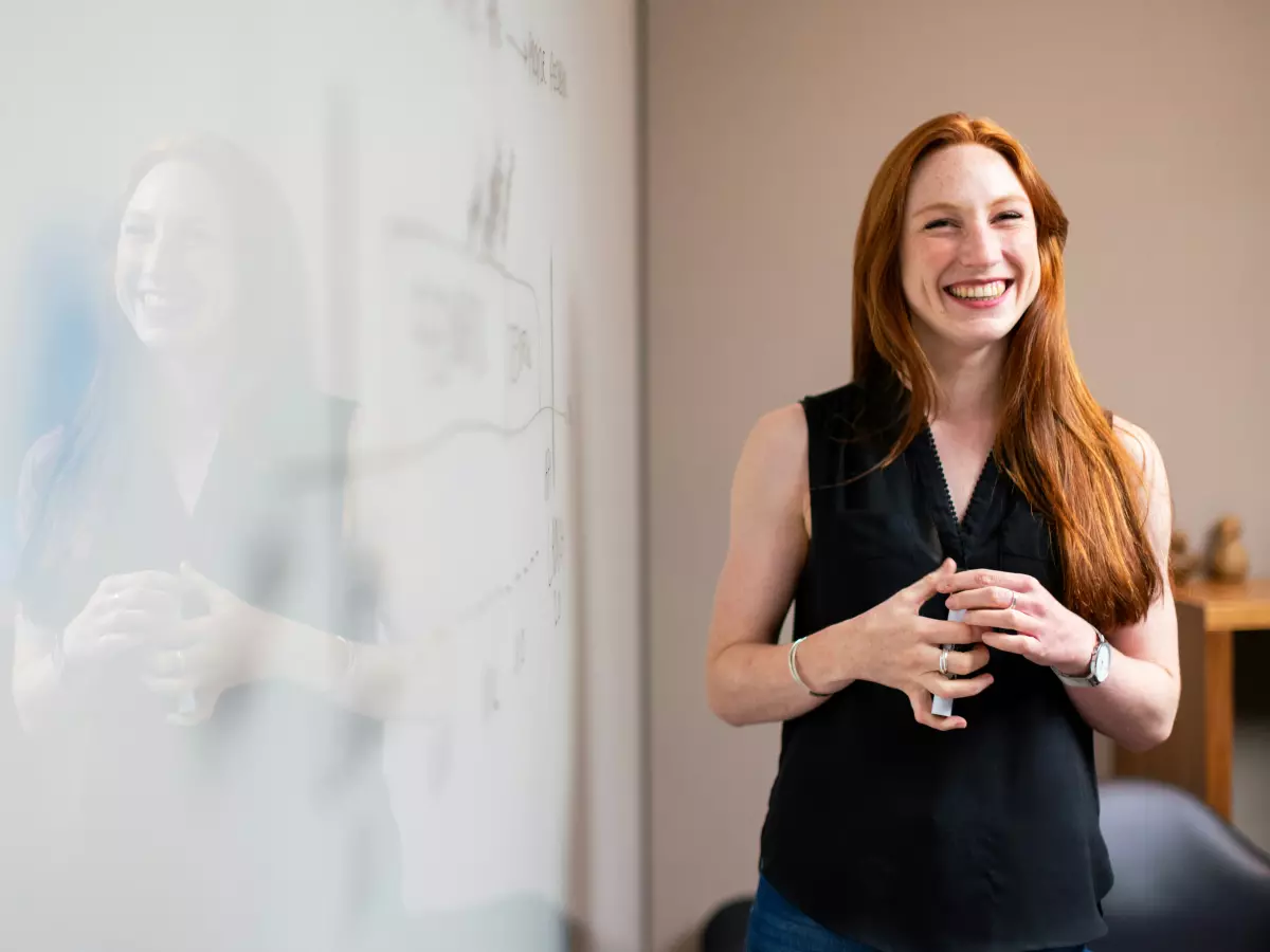 A woman is standing in front of a whiteboard, smiling.