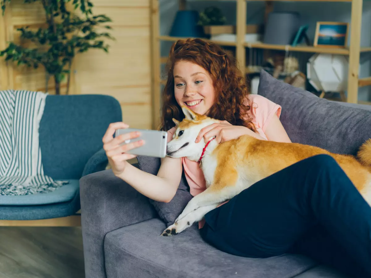 A young woman with red hair is taking a selfie with her dog on her lap.