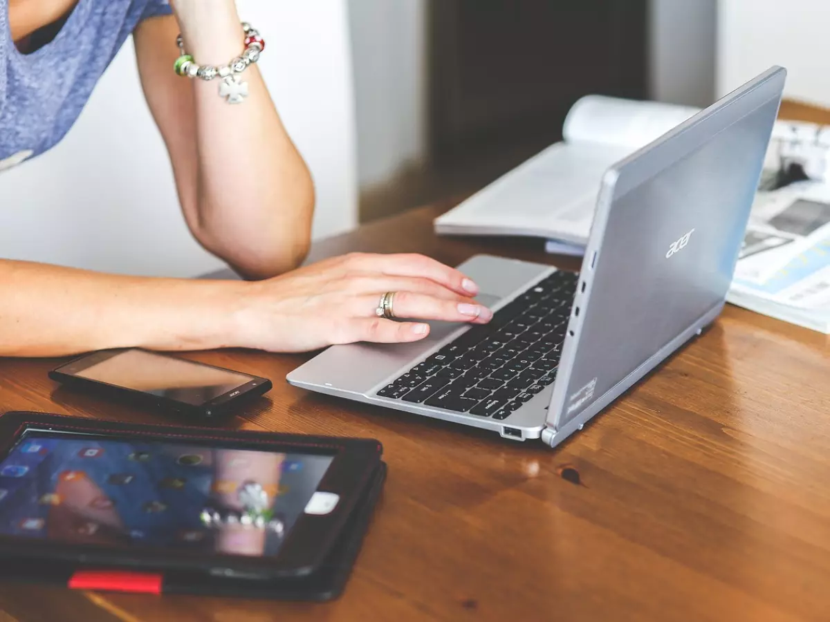 A person sitting at a desk, using a laptop. There are other electronic devices on the desk, including a phone and a tablet.