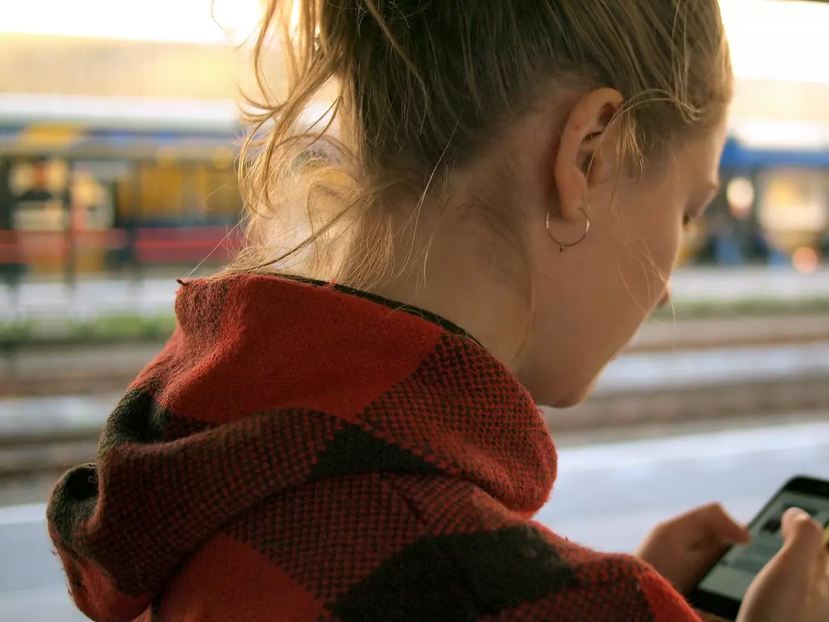 A young woman uses her smartphone on a train platform.