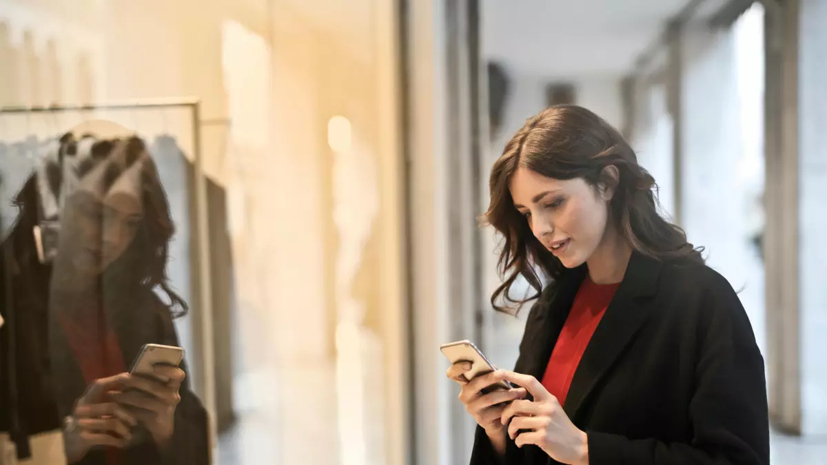 A woman stands in front of a shop window and uses a smartphone.