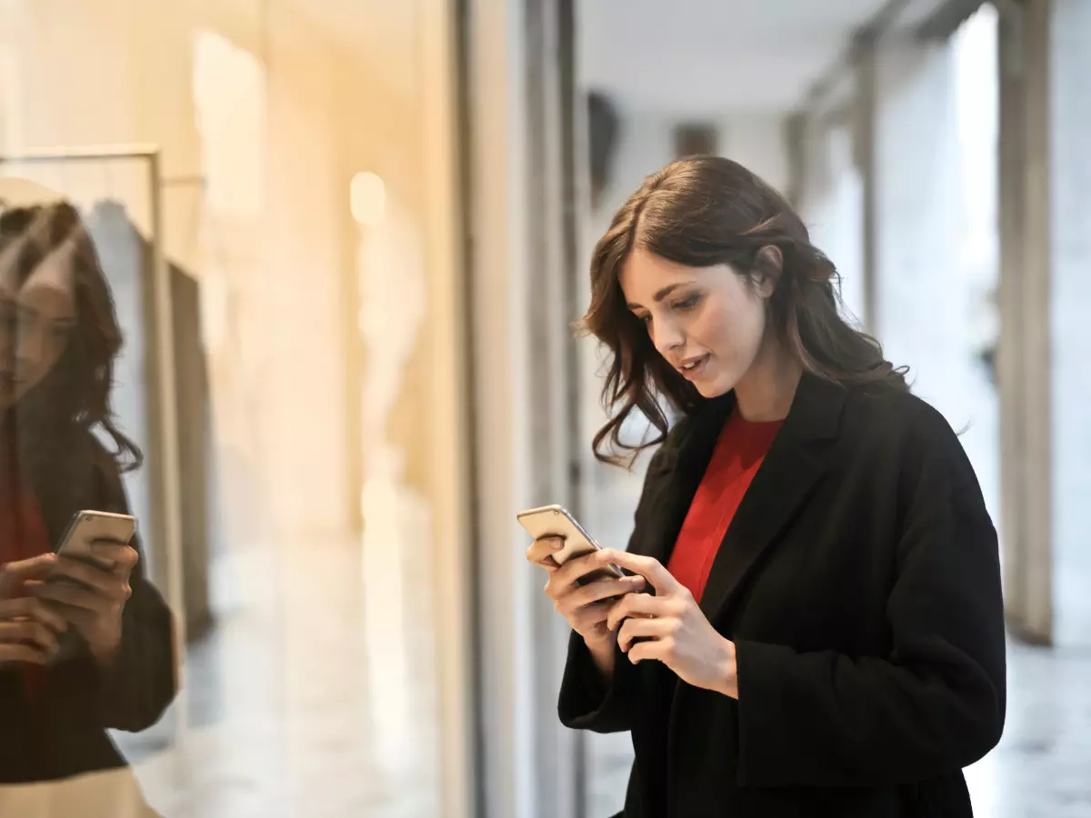 A woman stands in front of a shop window and uses a smartphone.