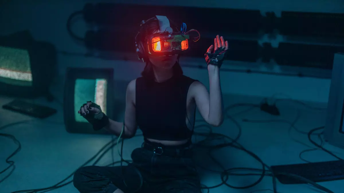 A person wearing a VR headset and gloves is sitting in front of multiple computer screens in a dark setting.