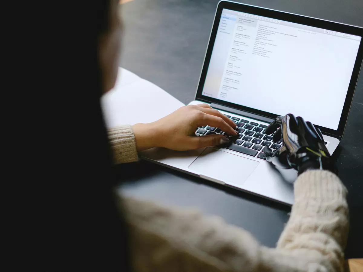 A person is typing on a laptop computer. The person is wearing a light-colored sweater. The laptop is sitting on a table. The background is out of focus.