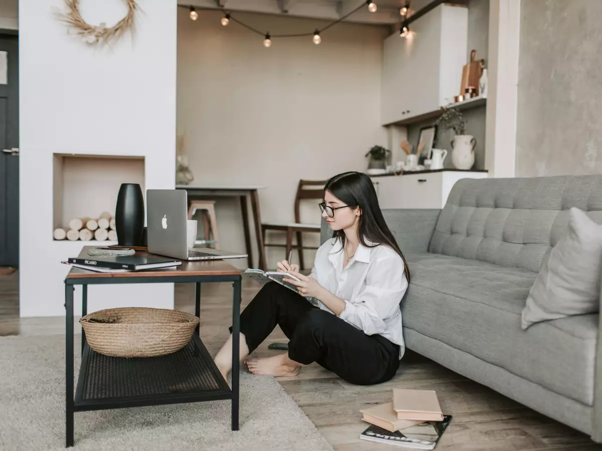 A young woman sits on the floor of a modern living room, using a laptop.  The room features muted colors and minimalist decor.