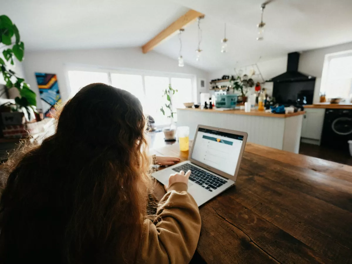 A young person is sitting at a table, looking at a laptop screen.