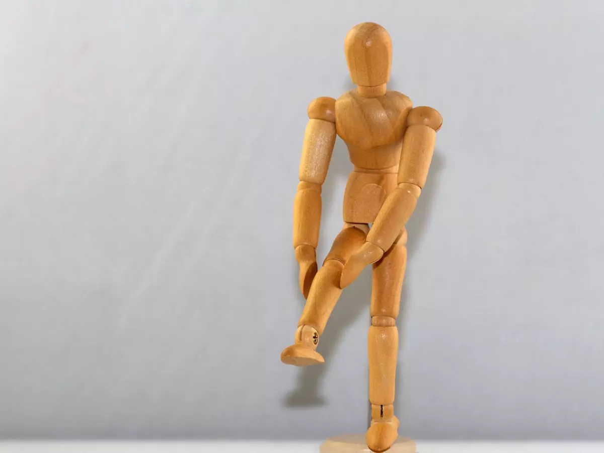 A wooden model of a person with its leg bent at the knee.