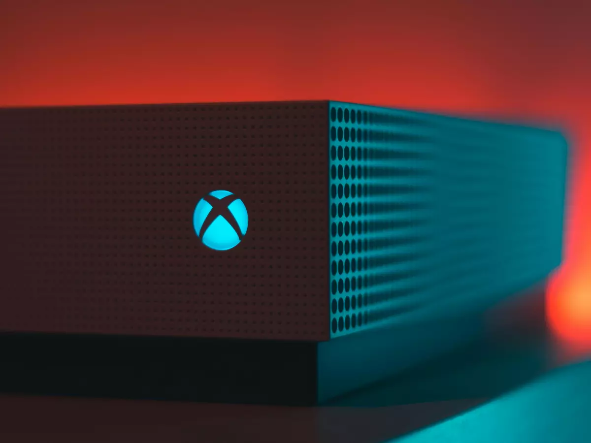 A close-up of the Xbox Series X console with a red background. The console is black with a blue light around the Xbox logo.