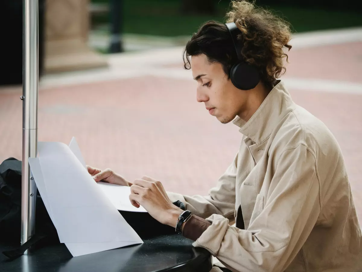 A person wearing headphones is sitting at a table, taking notes in a notebook.