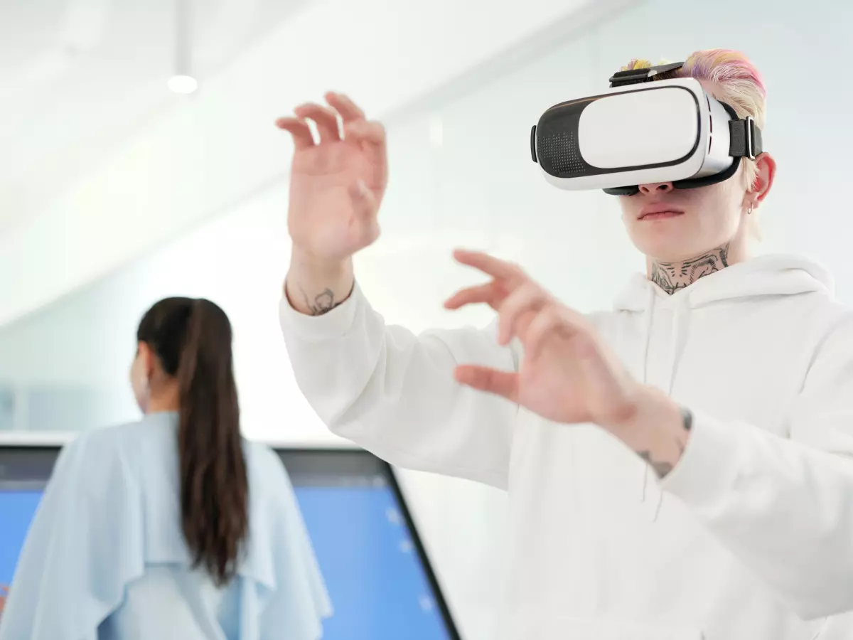 A man wearing a VR headset interacts with a virtual environment, with another person standing in the background.