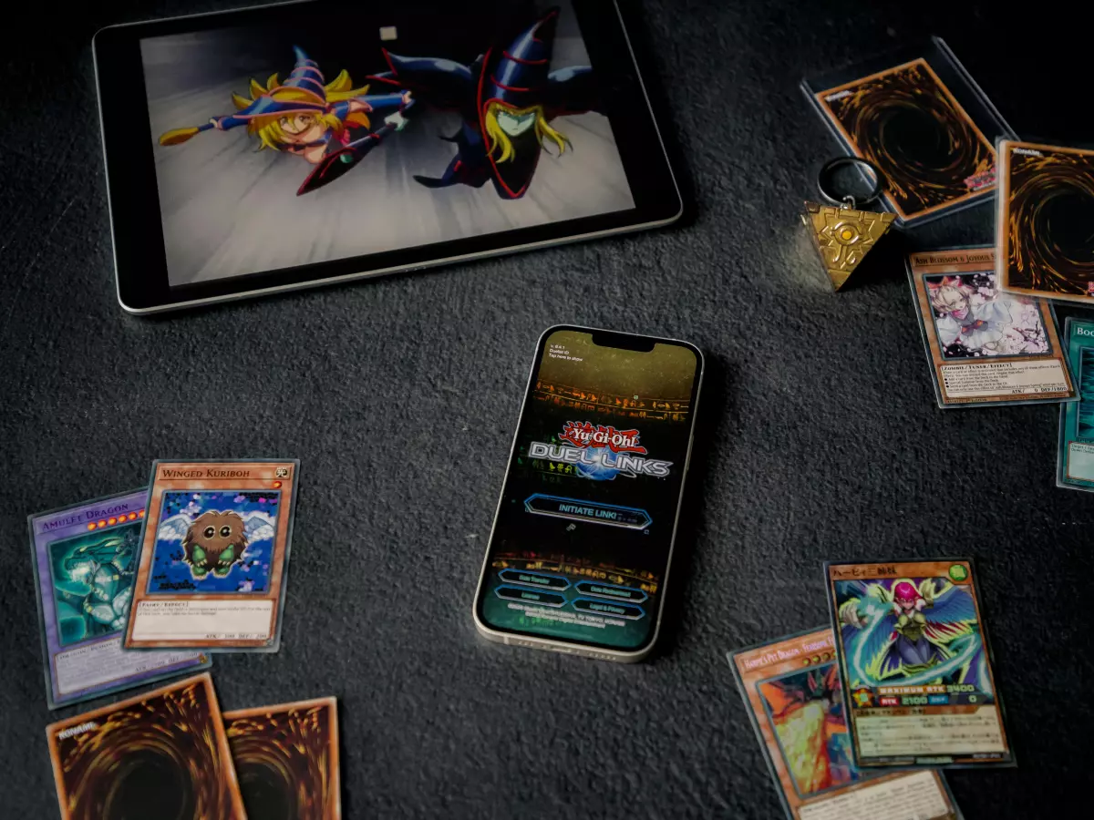 A close-up of a smartphone displaying a card game. The phone is surrounded by several scattered cards, while a tablet displaying a similar card game is in the background.